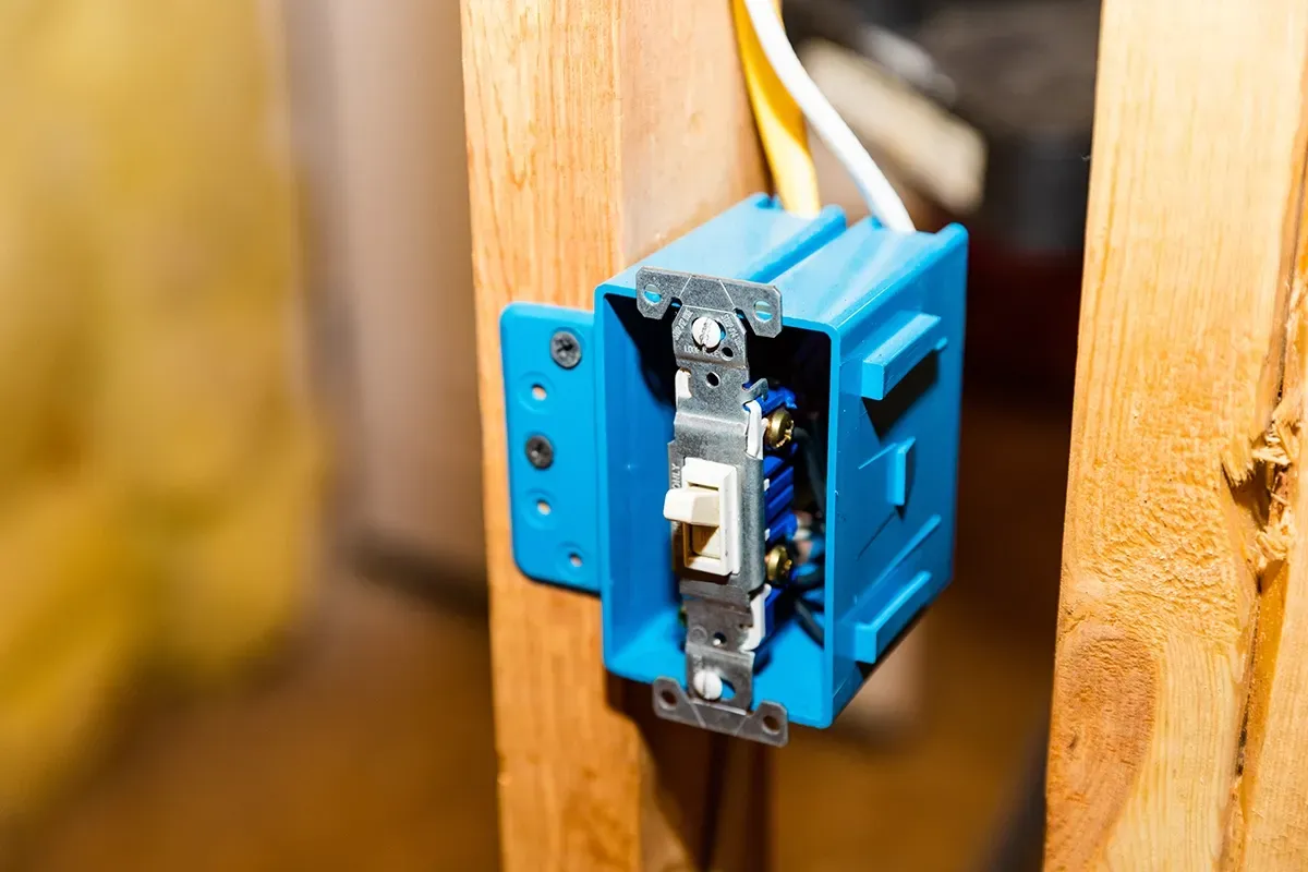 A wired light switch fitted in a blue electrical box on a timber stud, with cable running to it